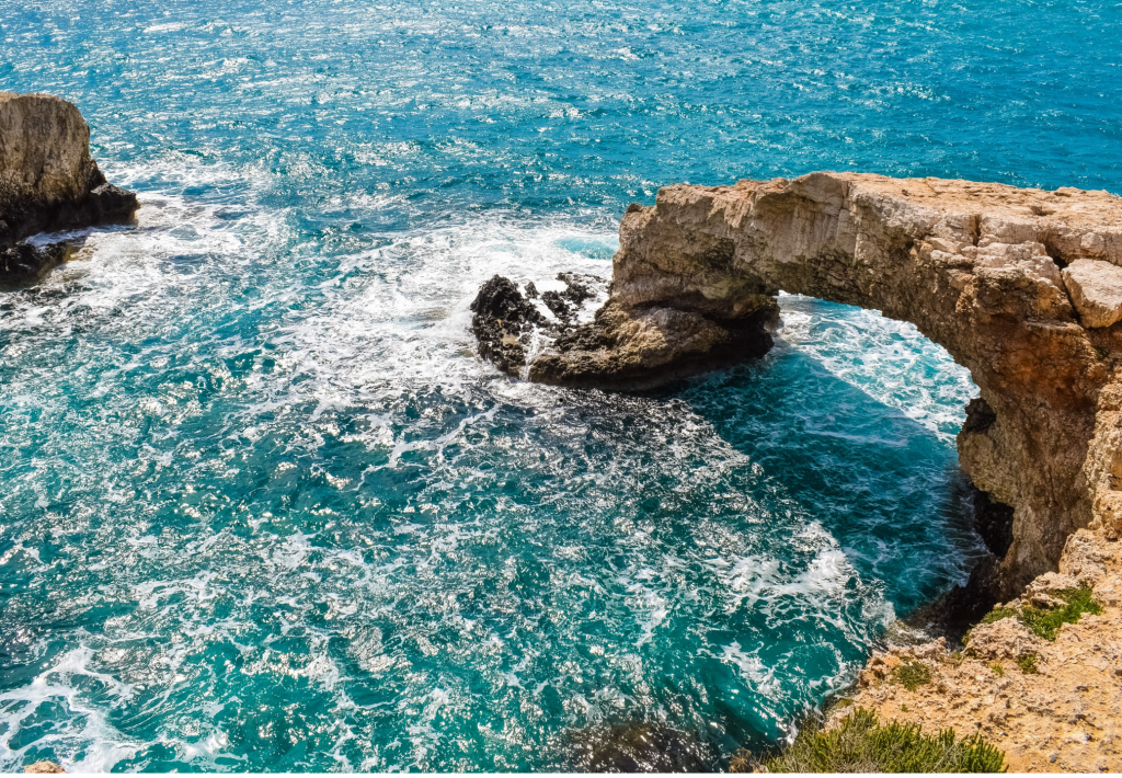 Natürliche Felsbrücke an der Küste Zyperns mit türkisblauem Meer und schäumenden Wellen. Die markante Felsformation zählt zu den bekanntesten Natursehenswürdigkeiten der Insel.